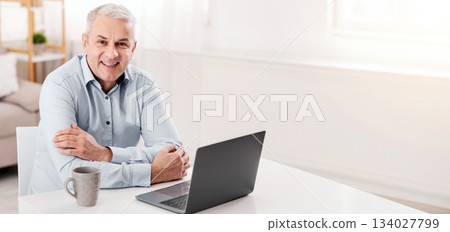 Remote Job. Smiling Mature Man Sitting At Desk With Laptop And Looking At Camera, Free Space 134027799