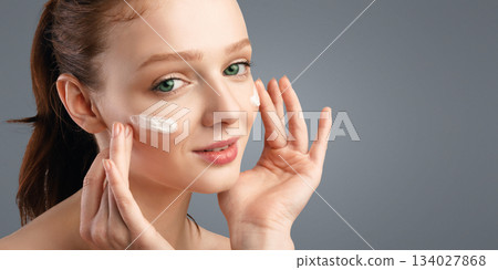 Closeup Of Red-Haired Young Woman Applying Moisturizing Cream On Face Caring For Skin Smiling To Camera Standing Posing On White Background. Studio Shot. Skincare For Young Lady Closeup Of Red-Haired Young Woman Applying Moisturizing Cream On Face Caring For Skin Smiling To Camera Standing Posing On White Background. Studio Shot. Skincare For Young Lady 134027868