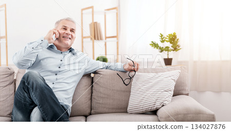 Communication Concept. Happy senior man calling his children, talking on mobile phone, resting on couch, copy space 134027876