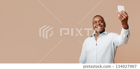 Handsome mature black man making selfie on cellphone and smiling, orange studio background Handsome mature black man making selfie on cellphone and smiling, orange studio background 134027907