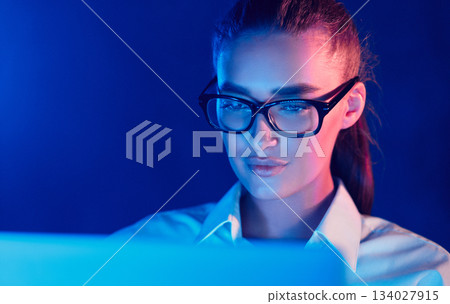 Night Online Work. Woman in glasses using laptop in colorful neon lights Night Online Work. Woman in glasses using laptop in colorful neon lights 134027915