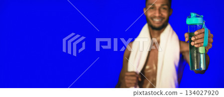 Workout Hydration. Black Athlete Man Offering Bottle Of Water To Camera Posing On Blue Studio Background. Shallow Depth, Selective Focus 134027920