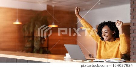 Lucky day. Emotional black woman looking at laptop, clenching fists and screaming, working at cafe, copy space Lucky day. Emotional black woman looking at laptop, clenching fists and screaming, working at cafe, copy space 134027924