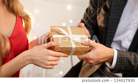 Gift With Love. Man giving box with present to his girlfriend on romantic dinner in restaurant, greeting with Valentine's Day or anniversary, closeup 134027930