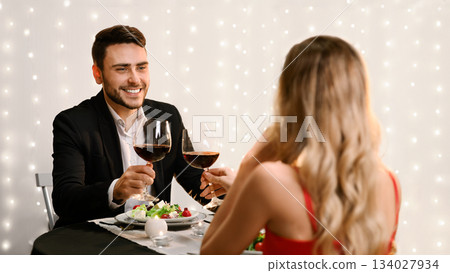 Toast For Us. Romantic couple clinking red wine glasses during Valentine Day dinner in restaurant. selective focus to man Toast For Us. Romantic couple clinking red wine glasses during Valentine Day dinner in restaurant. selective focus to man 134027934