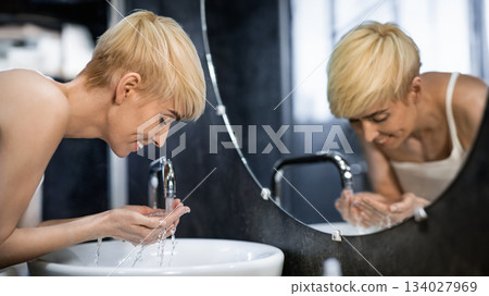 Cheerful Middle-Aged Lady Washing Face Standing In Bathroom. Hygiene And Skincare Routine. Selective Focus Cheerful Middle-Aged Lady Washing Face Standing In Bathroom. Hygiene And Skincare Routine. Selective Focus 134027969
