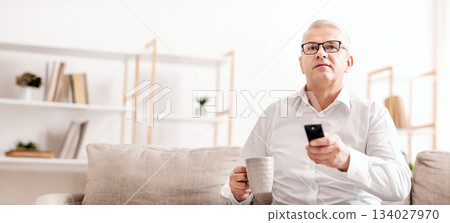 Smart Tv. Concentrated Senior Man Holding Remote Control And Coffee Mug, Empty Space, Low Angle View 134027970