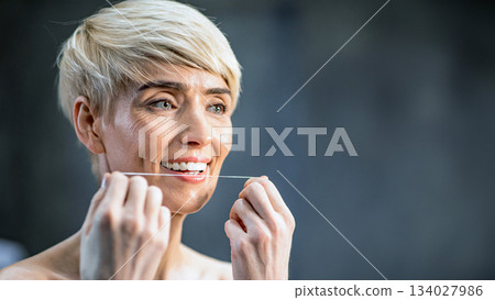 Toothcare Concept. Mature Lady Flossing White Teeth Standing Wrapped In Towel In Bathroom Indoor. Selective Focus, Copy Space Toothcare Concept. Mature Lady Flossing White Teeth Standing Wrapped In Towel In Bathroom Indoor. Selective Focus, Copy Space 134027986