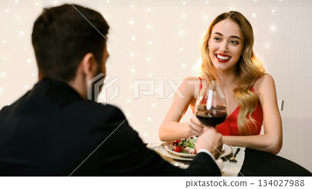 Happy Young Couple Clinking Red Wine Glasses On Romantic Dinner In Restaurant, Celebrating Anniversary Or Valentine's Day Together 134027988