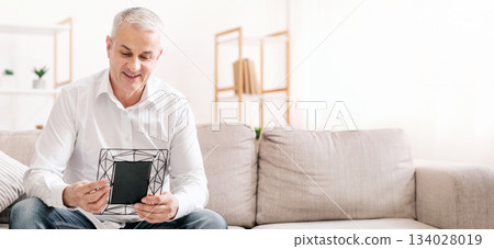 Memories Concept. Smiling elderly man holding photo frame, looking at picture Memories Concept. Smiling elderly man holding photo frame, looking at picture 134028019