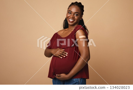 Safety vaccination during pregnancy cocnept. Cheerful pregnant young black woman got vaccinated against COVID-19, showing her arm with band on and hugging her big tummy, expecting baby, copy space Safety vaccination during pregnancy cocnept. Cheerful pregnant young black woman got vaccinated against COVID-19, showing her arm with band on and hugging her big tummy, expecting baby, copy space 134028023