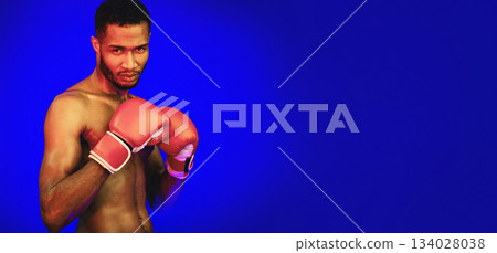 Shirtless Boxer In Boxing Gloves Standing In Ready-To-Fight Position Posing Looking At Camera On Blue Studio Background With Red Lights Shirtless Boxer In Boxing Gloves Standing In Ready-To-Fight Position Posing Looking At Camera On Blue Studio Background With Red Lights 134028038