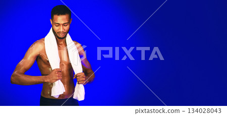 Black Muscular Guy Holding Towel Posing In Studio Over Blue Background. Sporty Lifestyle Concept. Copy Space Black Muscular Guy Holding Towel Posing In Studio Over Blue Background. Sporty Lifestyle Concept. Copy Space 134028043