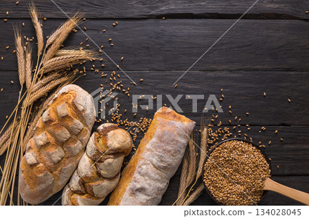 Bread border on wood with copy space background. Brown and white whole grain loaves still life composition with wheat ears scattered around. Bakery and grocery food store concept. 134028045