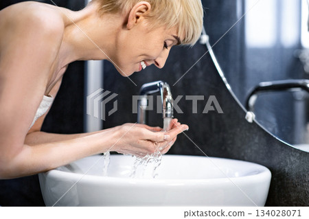 Joyful Mature Woman Washing Face Doing Morning Beauty Routine Standing Wrapped In Towel In Bathroom. Selective Focus Joyful Mature Woman Washing Face Doing Morning Beauty Routine Standing Wrapped In Towel In Bathroom. Selective Focus 134028071