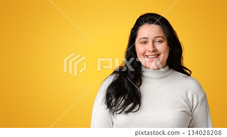 Portrait of happy millennial plump woman smiling at camera while posing on yellow background with copy space 134028208