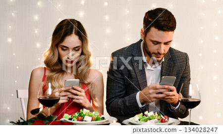 Social Media Addiction Concept. Couple spending time with their smartphones on romantic date in restaurant, ignoring each other Social Media Addiction Concept. Couple spending time with their smartphones on romantic date in restaurant, ignoring each other 134028247
