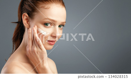 Facial Skincare For Teens. Ginger-Haired Girl Applying Face Cream Caring For Young Skin Looking At Camera Standing Posing In Studio Over White Background. Skin Care And Treatment For Youth Facial Skincare For Teens. Ginger-Haired Girl Applying Face Cream Caring For Young Skin Looking At Camera Standing Posing In Studio Over White Background. Skin Care And Treatment For Youth 134028315