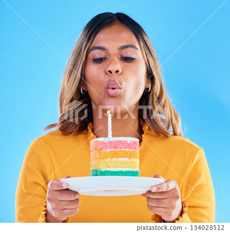 Birthday cake, candle blowing and woman in a studio with celebration and dessert. Party food, isolated and blue background of a young female with sweet and rainbow treat with surprise and plate Birthday cake, candle blowing and woman in a studio with celebration and dessert. Party food, isolated and blue background of a young female with sweet and rainbow treat with surprise and plate 134028512