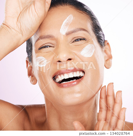 Face, cream and skincare of woman laughing in studio isolated on a purple background. Mature, portrait and funny female model with dermatology lotion, creme and moisturizer cosmetics for healthy skin 134028764