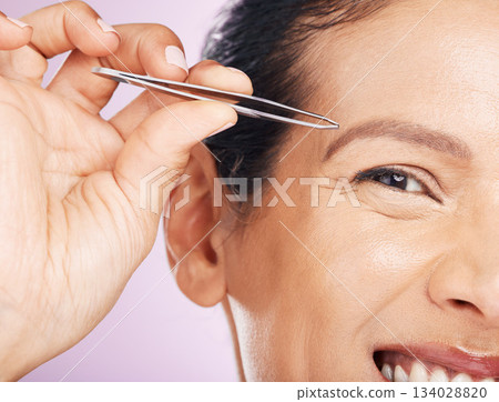 Woman with tweezers for plucking eyebrows in studio for mature facial hair removal routine. Self care, grooming and closeup of female model tweezing for face epilation treatment by purple background. 134028820