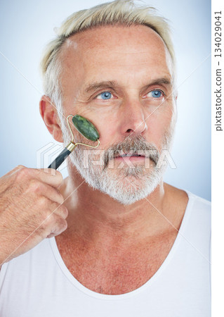 Senior man, jade roller and facial skincare with clean, self care and wellness in studio by white background. Elderly model, face skin massage or beauty with stone product, glow and dermatology detox Senior man, jade roller and facial skincare with clean, self care and wellness in studio by white background. Elderly model, face skin massage or beauty with stone product, glow and dermatology detox 134029041