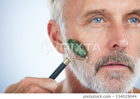 Senior man, jade roller and face for skin with smile, self care and wellness in studio by white background. Elderly model, facial massage and beauty glow with stone product, skincare and dermatology Senior man, jade roller and face for skin with smile, self care and wellness in studio by white background. Elderly model, facial massage and beauty glow with stone product, skincare and dermatology 134029044