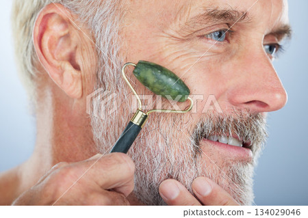 Elderly man, jade roller and face for skincare with smile, self care and wellness in studio by white background. Elderly model, facial massage and beauty with stone product, cosmetic and dermatology Elderly man, jade roller and face for skincare with smile, self care and wellness in studio by white background. Elderly model, facial massage and beauty with stone product, cosmetic and dermatology 134029046