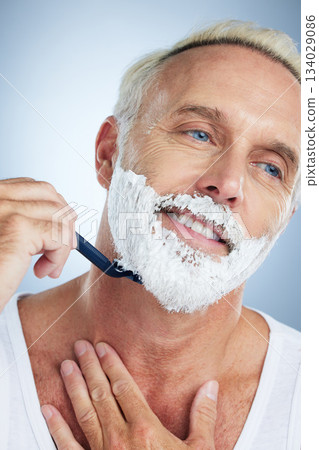 Senior man, face and razor shaving beard with cream for grooming, skincare or hair removal against a studio background. Happy mature male with shaver, creme or foam for hygiene or facial treatment 134029086