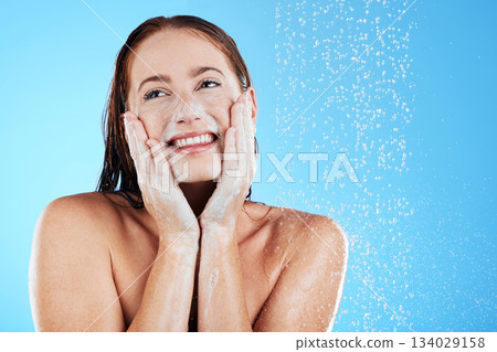 Shower, water and face of happy woman with soap in studio, blue background and skincare cleaning. Female model washing facial with foam, wet drops and beauty of self care, glow and smile on backdrop Shower, water and face of happy woman with soap in studio, blue background and skincare cleaning. Female model washing facial with foam, wet drops and beauty of self care, glow and smile on backdrop 134029158