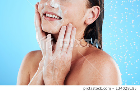 Woman face, wash and shower studio with a young female hands doing skincare and beauty routine. Bathroom, dermatology and facial treatment of a model smile from cleaning and isolated blue background Woman face, wash and shower studio with a young female hands doing skincare and beauty routine. Bathroom, dermatology and facial treatment of a model smile from cleaning and isolated blue background 134029183