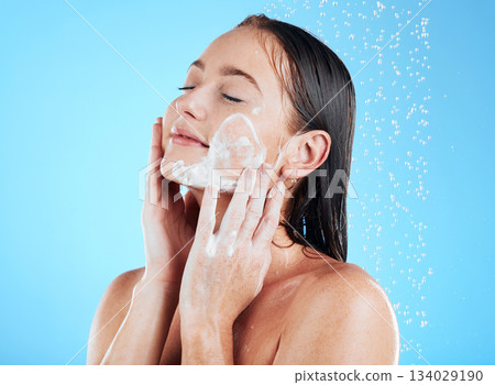 Shower, facial and woman washing face with soap on blue background for grooming, cleaning and wellness. Skincare, bathroom and happy girl with foam product for hygiene, hydration and beauty in studio 134029190