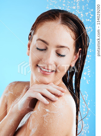 Water, soap and woman washing or shower in studio for skincare, wellness and clean body or self care. Happy female aesthetic model splash for cleaning, hygiene and skin cosmetics on blue background 134029200