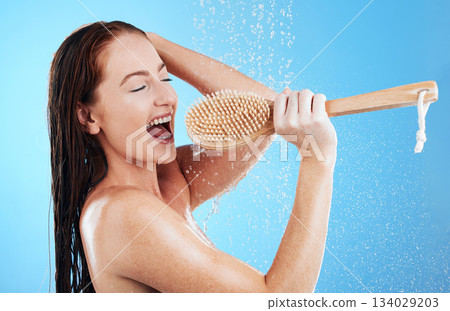 Shower singing, skincare and woman with happiness and fun in a studio. Bathroom, music and happy female model with isolated blue background and cleaning brush karaoke for beauty routine and wellness 134029203