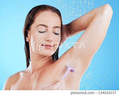 Woman in shower, grooming and shaving armpit, hygiene and water drops with razor and clean on blue background. Skincare, hydration and hair removal with female cleaning body, eyes closed and calm Woman in shower, grooming and shaving armpit, hygiene and water drops with razor and clean on blue background. Skincare, hydration and hair removal with female cleaning body, eyes closed and calm 134029237