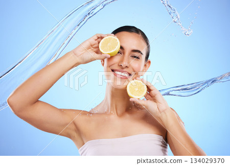 Vitamin c, lemon and water splash with portrait of woman in studio for natural cosmetics, nutrition and detox. Glow, fruits and hydration with female on blue background for diet, face and skincare 134029370