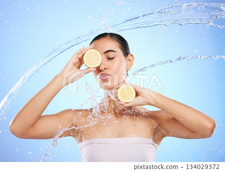 Beauty, water splash and lemon with woman in studio for natural cosmetics, nutrition and detox. Glow, fruits and hydration with female and pouting on blue background for vitamin c, face and skincare Beauty, water splash and lemon with woman in studio for natural cosmetics, nutrition and detox. Glow, fruits and hydration with female and pouting on blue background for vitamin c, face and skincare 134029372