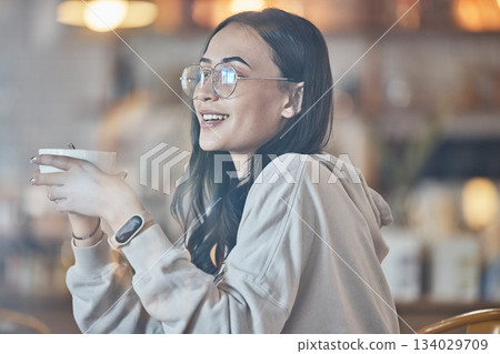 Thinking, happy and a woman drinking coffee in a cafe to relax alone over the weekend behind glass. Idea, smile and caffeine with an attractive young female enjoying a beverage in a restaurant 134029709