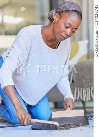 Maid, housekeeping and black woman cleaning and sweeping floor of a living room in a home or house for hygiene. Housekeeper, cleaner and domestic female remove dirt or dust with hand broom 134029745