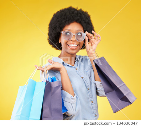 Fashion, thinking and black woman with shopping bags, smile and excited for sale in studio on yellow background. Shopper, girl and cool customer cheerful for boutique, retail or store discount 134030047