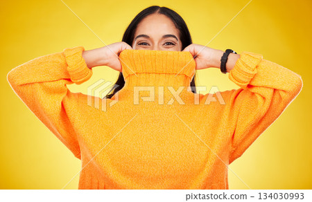 Happy, cover and portrait of a woman with a jersey isolated on a yellow background in a studio. Hiding, winter and a girl holding a jumper up for covering, warmth and bad weather on a backdrop Happy, cover and portrait of a woman with a jersey isolated on a yellow background in a studio. Hiding, winter and a girl holding a jumper up for covering, warmth and bad weather on a backdrop 134030993