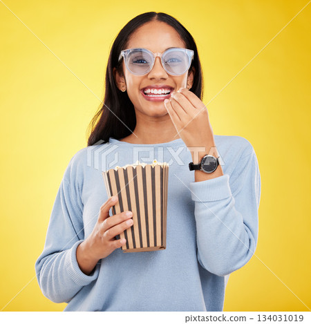 Woman is eating popcorn, watching tv and happy in portrait with snack for movie on yellow studio background. Streaming service, cinema and food with corn treat, female smile with funky sunglasses Woman is eating popcorn, watching tv and happy in portrait with snack for movie on yellow studio background. Streaming service, cinema and food with corn treat, female smile with funky sunglasses 134031019