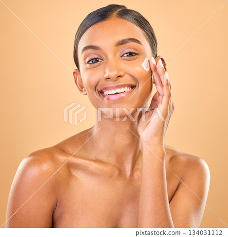 Face portrait, skincare and woman with cream in studio isolated on a brown background. Dermatology smile, cosmetics and happy Indian female model apply lotion, creme and moisturizer for healthy skin. Face portrait, skincare and woman with cream in studio isolated on a brown background. Dermatology smile, cosmetics and happy Indian female model apply lotion, creme and moisturizer for healthy skin. 134031112