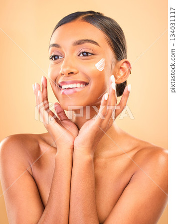 Face, skincare smile and woman with cream in studio isolated on a brown background. Dermatology cosmetics, thinking and happy Indian female model apply lotion, creme and moisturizer for healthy skin. Face, skincare smile and woman with cream in studio isolated on a brown background. Dermatology cosmetics, thinking and happy Indian female model apply lotion, creme and moisturizer for healthy skin. 134031117