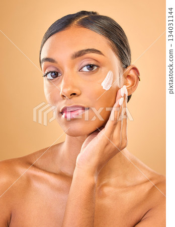 Face portrait, skincare and woman with cream in studio isolated on a brown background. Dermatology, cosmetics or confident Indian female model with lotion, beauty creme or moisturizer for skin health 134031144