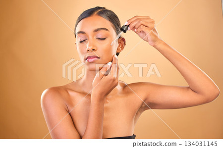 Face, skincare serum and woman with eyes closed in studio isolated on brown background. Dermatology, cosmetics and Indian female model apply hyaluronic acid, retinol or essential oil for healthy skin 134031145