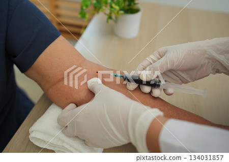 Close up of doctor or nurse taking blood sample from arm vein with vacutainer. syringe to venipuncture the patient Close up of doctor or nurse taking blood sample from arm vein with vacutainer. syringe to venipuncture the patient 134031857