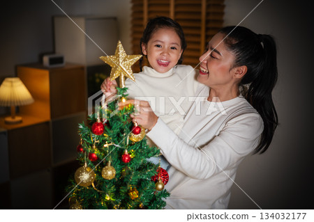 mother and toddler girl decorating star on Christmas tree in home at night 134032177