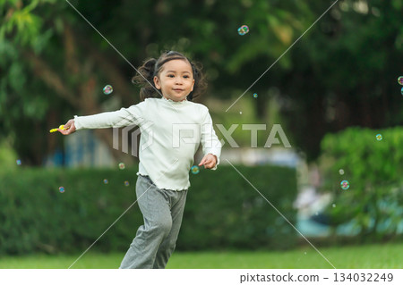 happy toddler girl running and playing soap bubble in park 134032249