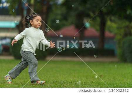 happy toddler girl running and playing soap bubble in park 134032252